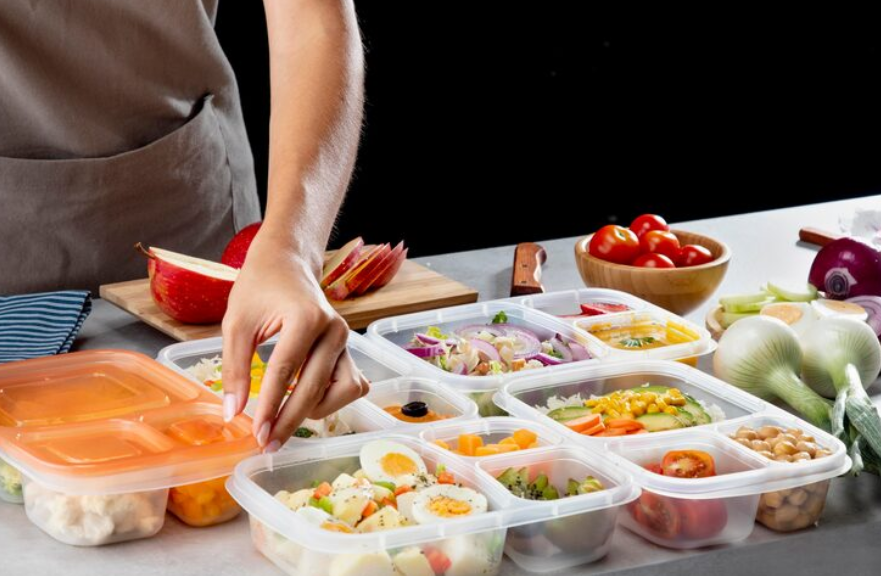 person portioning meals into containers to prep a week of lunches in a home kitchen