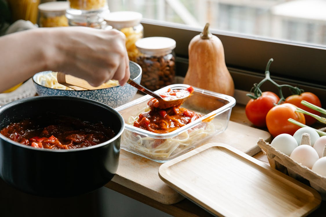 person portioning pasta into a container for meal prep for beginners in a home kitchen