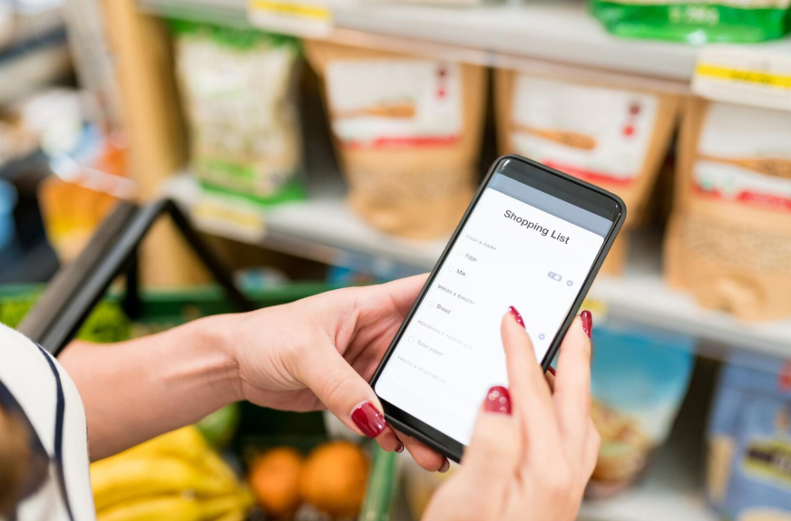 shopper using a phone to check the best grocery apps for saving money and time during a grocery trip
